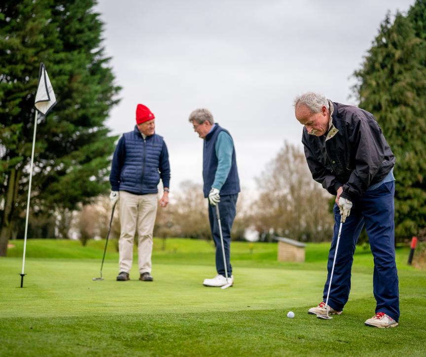 A mature group on the golf course putting.